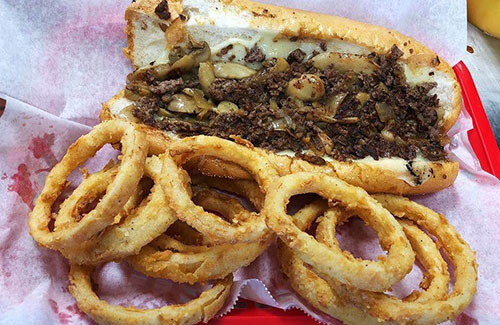 Philly cheesesteak with grilled onions served with onion rings