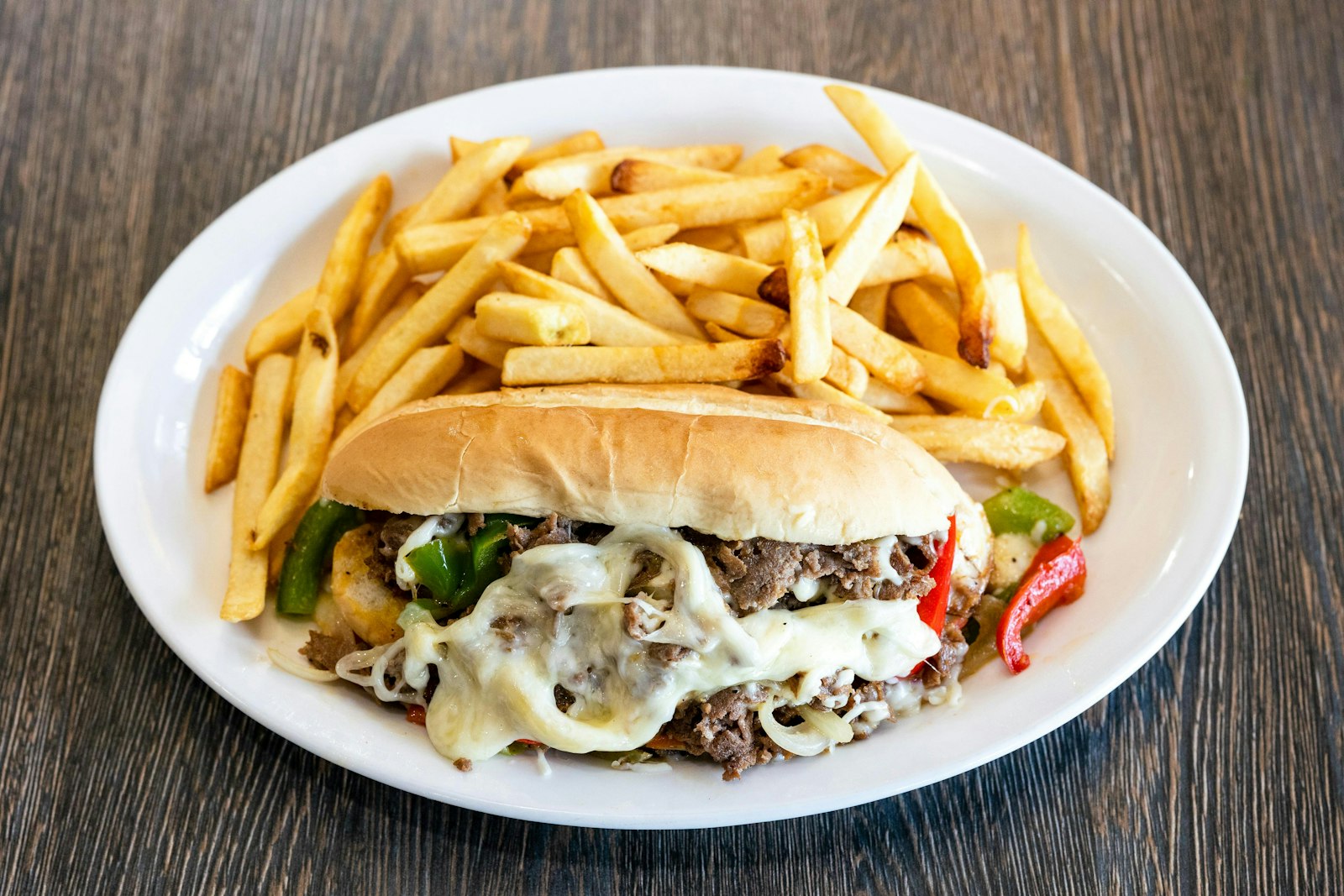 Philly cheesesteak with melted cheese and peppers served with fries